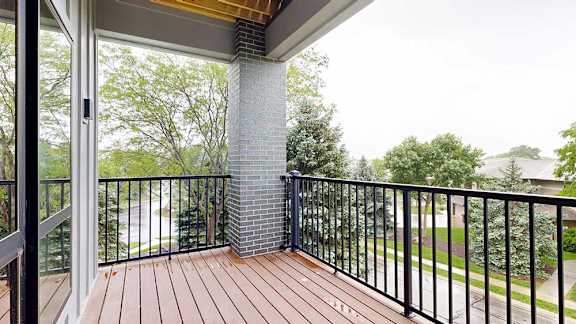 A balcony with a metal railing, a brick pillar, and a view of the neighborhood.