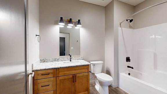 A bathroom with a quartz vanity, warm wooden cabinets, and a tub shower with black fixtures.