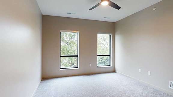 A carpeted bedroom with a ceiling fan and floor-to-ceiling windows.