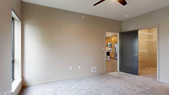 A bedroom with floor-to-ceiling windows, a ceiling fan, and a walk-in closet.
