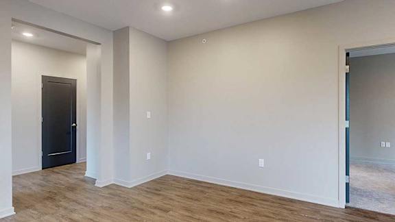 A living room with hardwood-style flooring and a hallway to the front entryway.