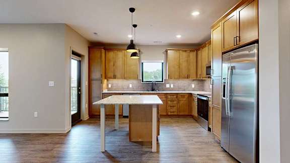 A kitchen with warm wooden cabinets, quartz countertops, an island, and stainless steel appliances.