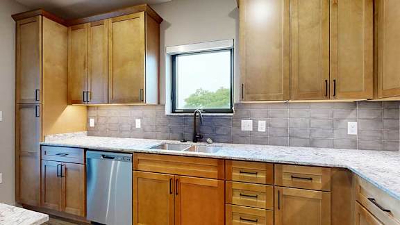 A kitchen with warm wooden cabinets, quartz countertops, a tile backsplash, and a window over the kitchen sink.
