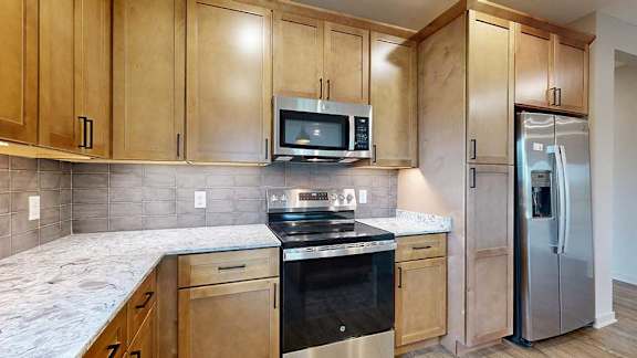 A close up of the stainless steel microwave and range in a kitchen with warm wooden cabinets.