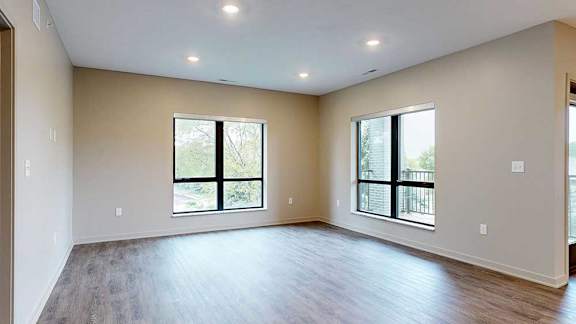 A living room with hardwood-style flooring and floor-to-ceiling windows.