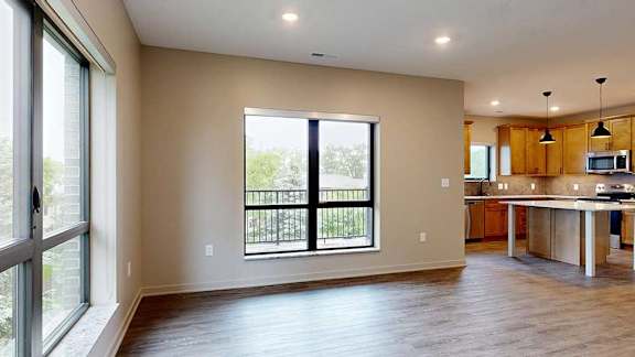 A living room with floor-to-ceiling windows open to a kitchen with a large island with warm wooden cabinets.