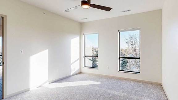 a bedroom with carpeted flooring, two windows, and a ceiling fan