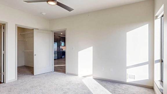 a bedroom with a carpeted floor, a ceiling fan, a large window, and a spacious walk-in closet