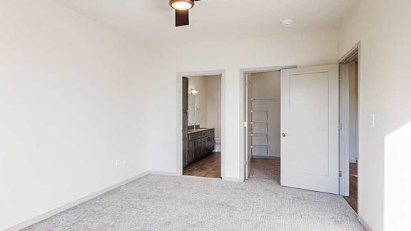 a bedroom with a carpeted floor, a ceiling fan, an attached bathroom, and a spacious walk-in closet