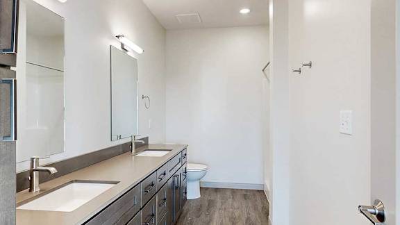 a bathroom with a quartz double vanity sink, a mirror with overhead lighting, and a walk-in shower