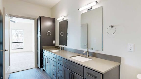 a bathroom with a double vanity sink, two mirrors, and a tall storage cabinet