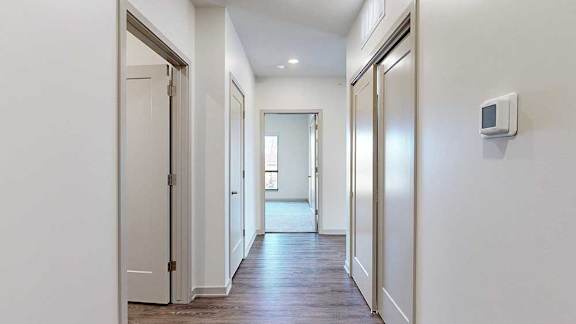 a hallway leading to a bedroom with doors on either side to the bathroom and a closet