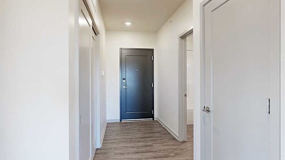 a hallway leading to front door with doors on either side to the bathroom and a closet