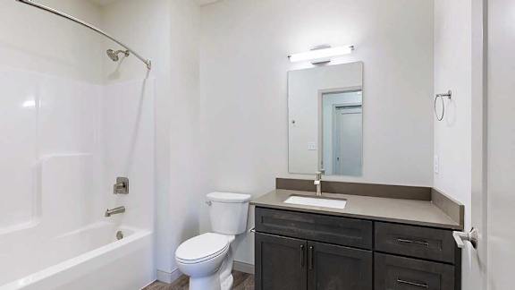 a bathroom with a quartz vanity sink, a mirror with overhead lighting, and a combination shower and tub