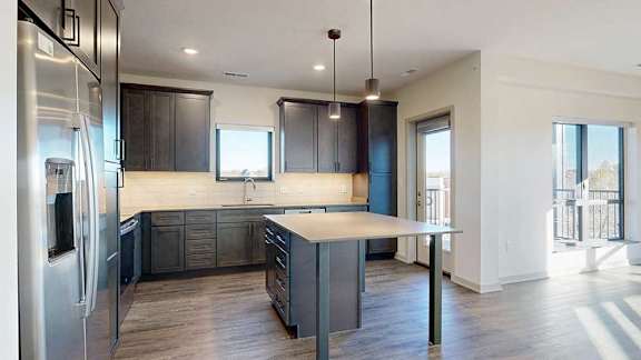 a modern kitchen with dark wooden cabinets, quartz countertops, a tile backsplash, a large central island, and stainless steel appliances