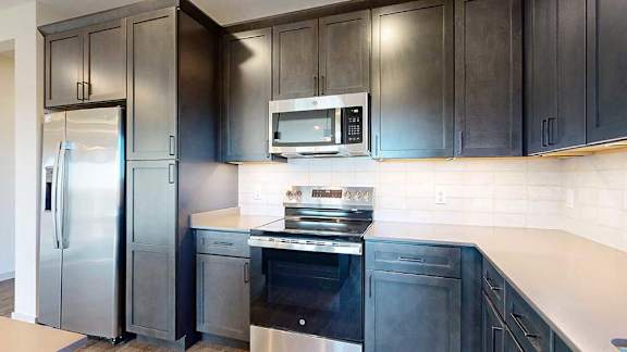 a modern kitchen with dark wooden cabinets, quartz countertops, a tile backsplash, and stainless steel appliances