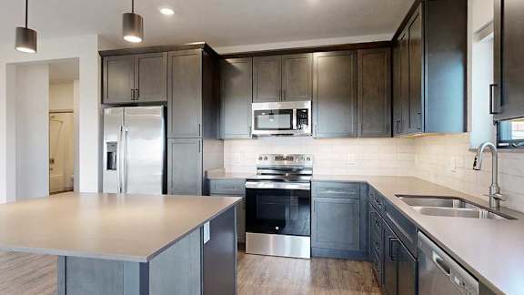 a modern kitchen with dark wood cabinets, quartz countertops, a tile backsplash, and stainless steel appliances