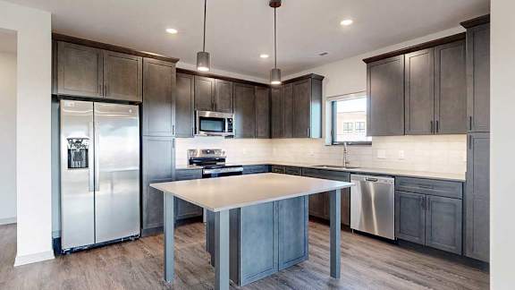 a modern kitchen with dark wooden cabinets, quartz countertops, a tile backsplash, a large central island, and stainless steel appliances