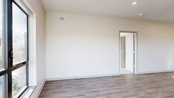 a living room with a large window, hardwood flooring, and a door to a bedroom