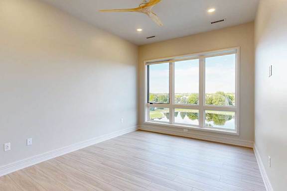 Penthouse bedoom with a ceiling fan and a large window with a view of the pond.