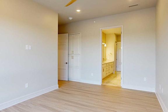 A penthouse bedroom with a white walls and a light warm brown wood floor.