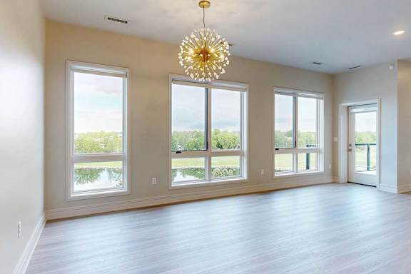 A large, empty living room with a chandelier and large windows overlooking the pond