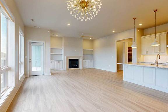 A spacious living room with a fireplace and a kitchen area in the background.