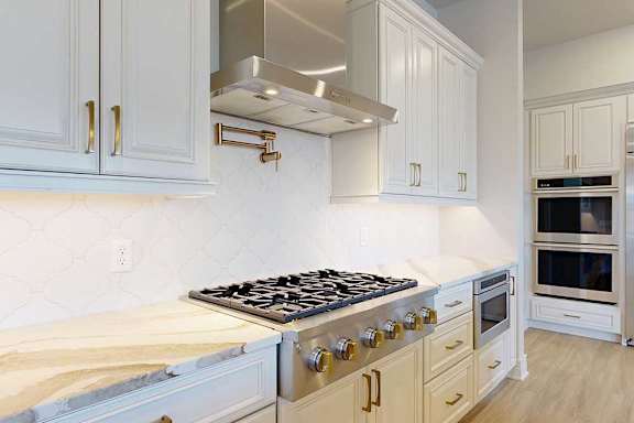 Kitchen with custom white cabinets, premium gas appliances, and a pot filler