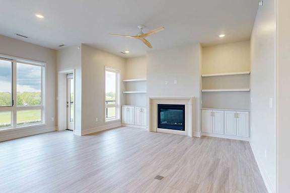 A spacious living room with a fireplace, built-in shelving, and a ceiling fan.