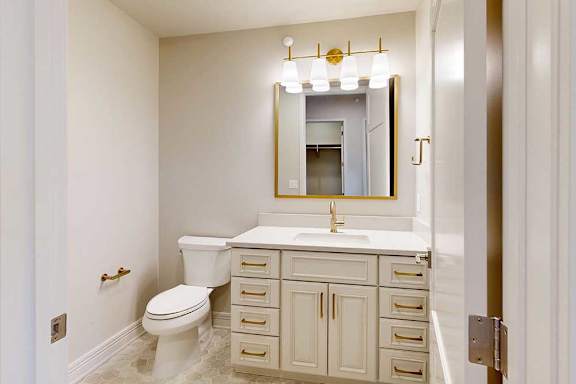 Penthouse hall bathroom with white cabinets, marble tile floors, and gold hardware finishes