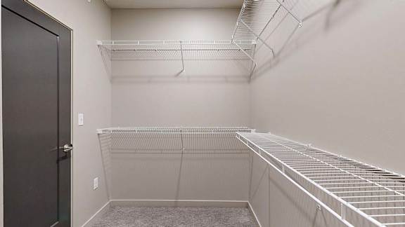 Spacious apartment walk-in closet with built-in wire shelving on multiple walls, neutral finishes, and carpeted flooring for organized storage.