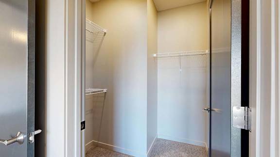 Bright apartment walk-in closet with built-in wire shelving and an adjacent glass-enclosed shower, featuring neutral walls and wood-look flooring.