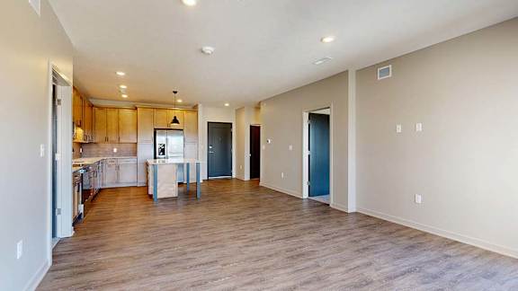 Spacious open-concept apartment living area with wood-look flooring, recessed lighting, and a modern kitchen featuring a center island, wood cabinetry, and stainless steel appliances.