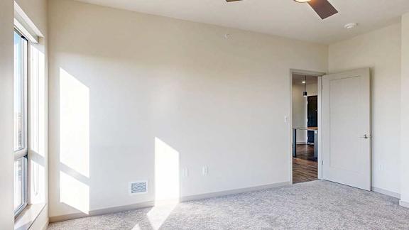 a bedroom with a window shining in, carpeted flooring, and a ceiling fan