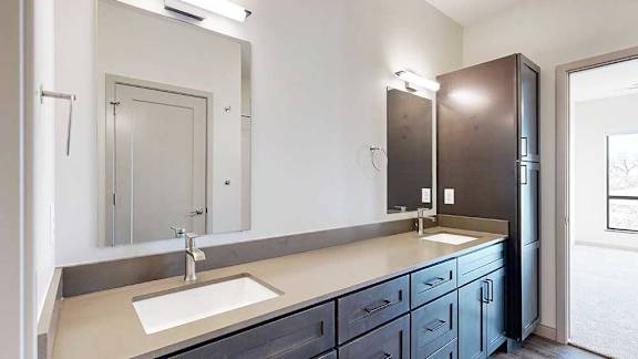 a bathroom with a double vanity sink, two mirrors, and a tall dark wooden storage cabinet