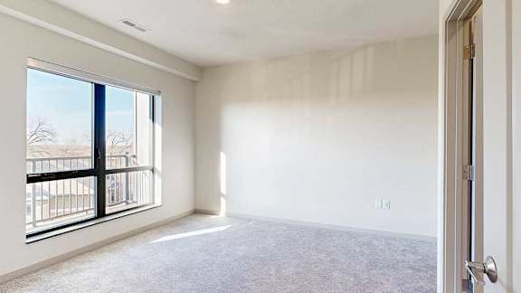 a bedroom with carpeted flooring and a window looking out to a balcony