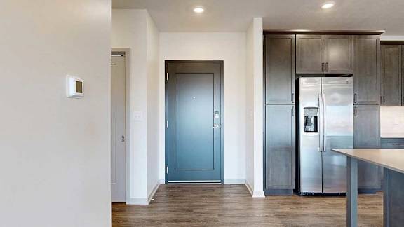 a grey front door next to a modern kitchen with dark cabinets and stainless steel appliances