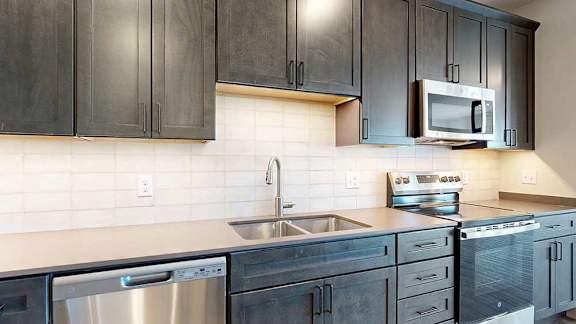 a kitchen with dark cabinets, quartz cabinets, a tile backsplash, and stainless steel appliances
