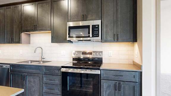 a modern kitchen with dark cabinets, a tile backsplash, quartz countertops, and stainless steel appliances