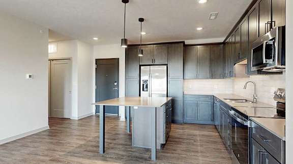 a grey front door next to a modern kitchen with dark cabinets, a central table island, and quartz countertops