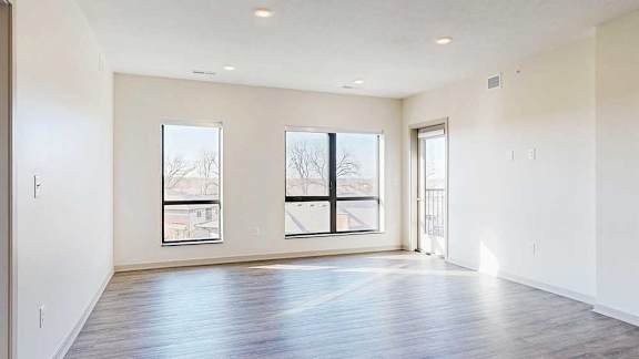 a spacious living room with two large windows, hardwood flooring, and a windowed door to a balcony