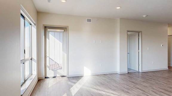 a spacious living room with a windowed door to a balcony and a door to a bedroom