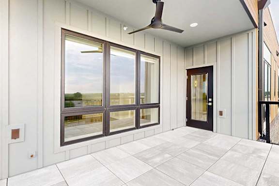 An oversized balcony with a floor-to-ceiling window to the living room, stone tile flooring, a ceiling fan, and a windowed door to the living room.
