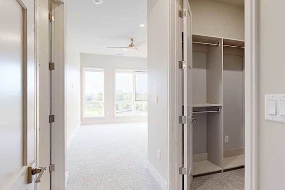 A carpeted with floor-to-ceiling windows, a ceiling fan, and a walk-in closet with built-in wooden shelving.