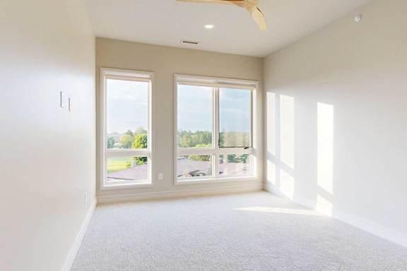 A carpeted with floor-to-ceiling windows and a ceiling fan.