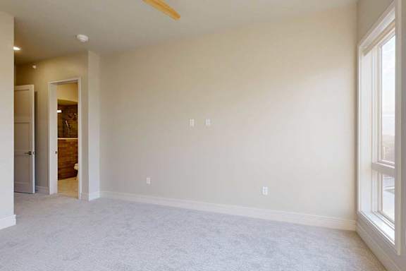 A carpeted bedroom with floor-to-ceiling windows, a ceiling fan, and ensuite bathroom.