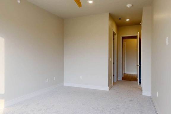 A spacious carpeted bedroom with a ceiling fan, attached bathroom, and walk-in closet.