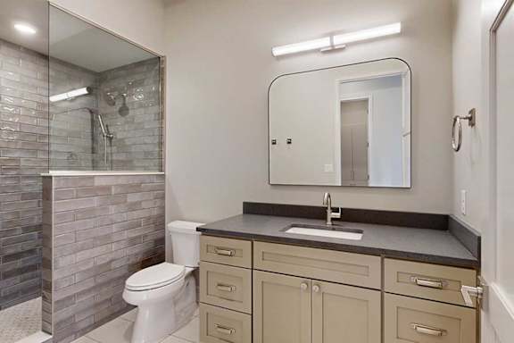 A bathroom with a wide quartz vanity sink, a modern framed mirror with overhead lighting, and a tiled walk-in shower with a half wall and glass window.