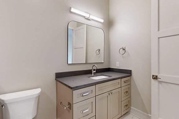 A bathroom with a wide quartz vanity sink, a framed mirror, and overhead lighting.