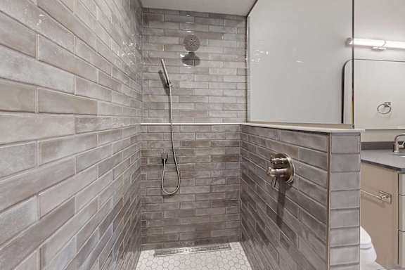 A tiled walk-in shower with a half wall, glass window, and a shower head with detached sprayer.